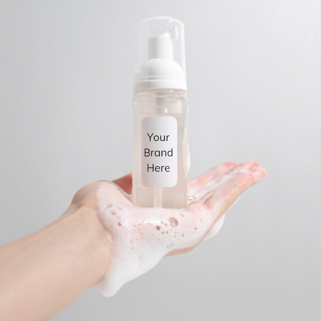 a hand covered with foaming cleanser outstretched with a foaming pump bottle in the palm which reads Your Brand Here