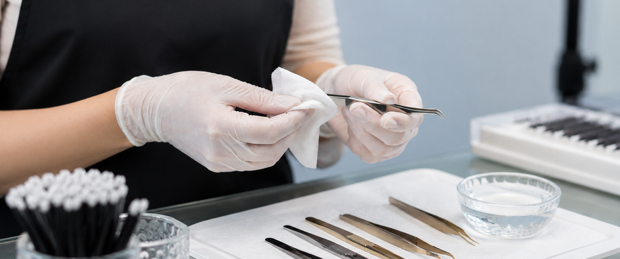 Gloved lash artist sanitising isolation tweezers