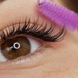 Close-up of eye with full eyelash extensions being brushed with a pink spoolie