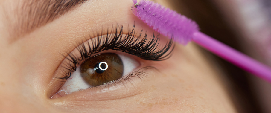 Close-up of eye with full eyelash extensions being brushed with a pink spoolie