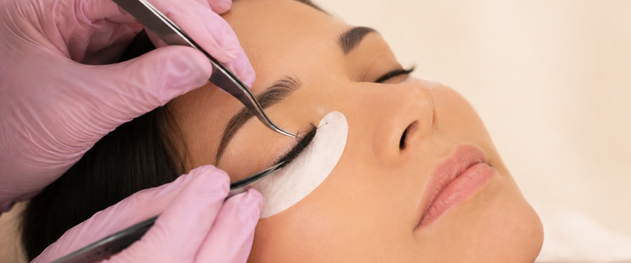 Gloved lash technician inspecting extensions with tweezers.