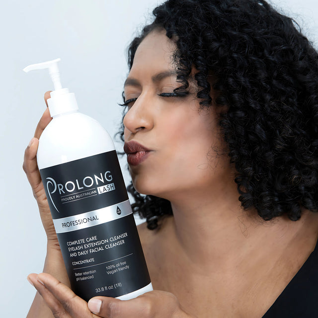 a women gently holding a large bottle of prolong lash cleanser, she has he eyes closed and she is leaning in to give the bottle a kiss