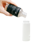 Hand pouring a white liquid from a Prolong bottle into a white container on a white background