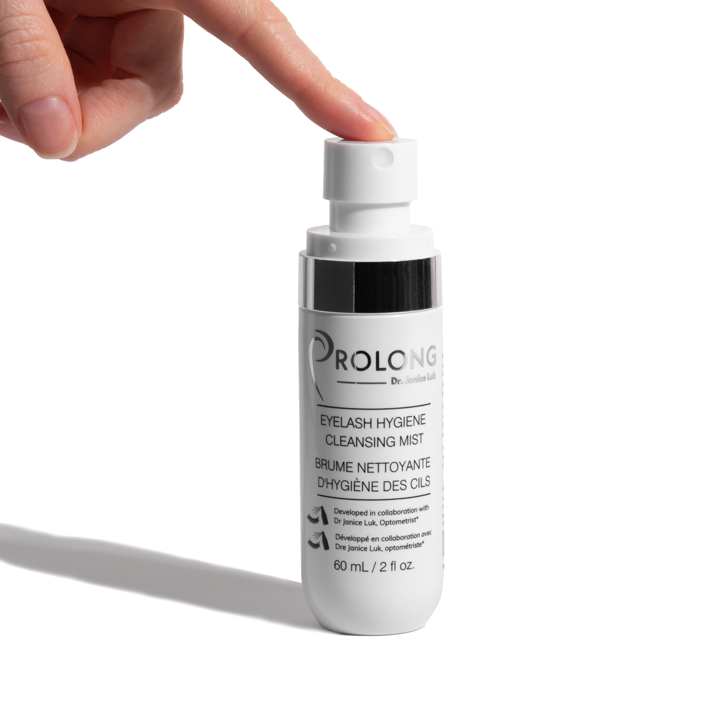 A hand presses the pump of a white bottle labeled Prolong Dr. Janice Luk Eyelash Hygiene Cleansing Mist against a clean white background.